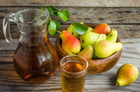 Pears in a wooden dish and a carafe of pear juice on wooden backgroundの写真素材