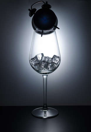 Wine glass filled with ice cubes and standing on the clock in the shadeの写真素材