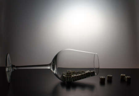 A fallen glass and a scattering of dice on a grey backgroundの写真素材