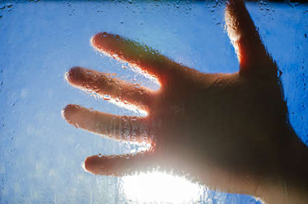 Man's hand on the background of bright light through the wet glass with dropsの写真素材