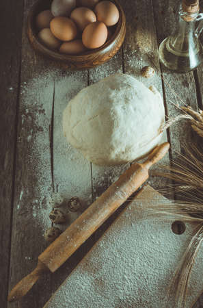 Kneaded dough, ears of wheat,rolling pin, eggs and a bottle of oil on the old rustic table closeupの写真素材