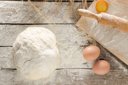Kneaded dough, ears of wheat,rolling pin, eggs and a bottle of oil on the old rustic table closeupの写真素材