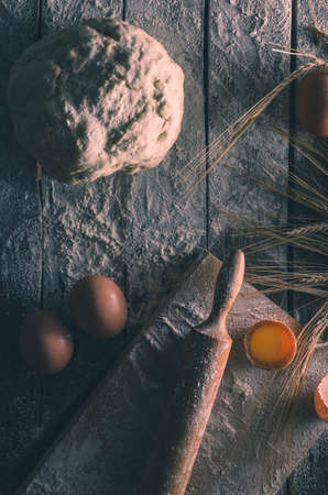 Kneaded dough, ears of wheat,rolling pin, eggs and a bottle of oil on the old rustic table closeupの写真素材