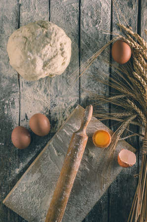 Kneaded dough, ears of wheat,rolling pin, eggs and a bottle of oil on the old rustic table closeup