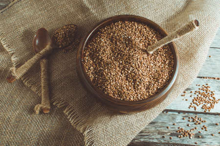 Buckwheat in a wooden bowl and a spoon full of buckwheat on the old wooden backgroundの写真素材