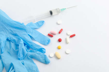 Blue medical gloves, syringe and pills with pills on white backgroundの写真素材