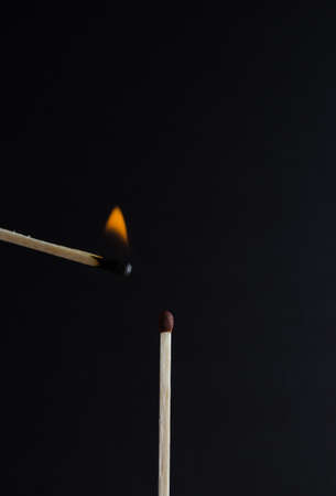 Burning match approached to an unlit match on black backgroundの写真素材