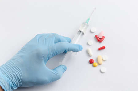 The hand of the medical worker in blue gloves holding a syringe on a light background and tablets assorted colorsの写真素材