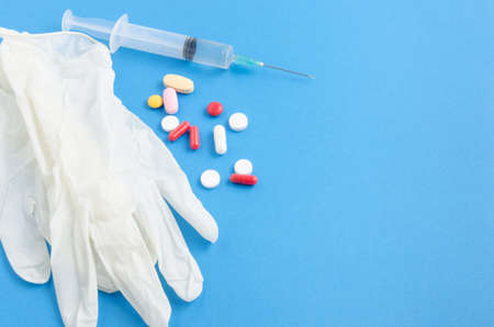 White medical gloves, syringe and pills on blue backgroundの写真素材