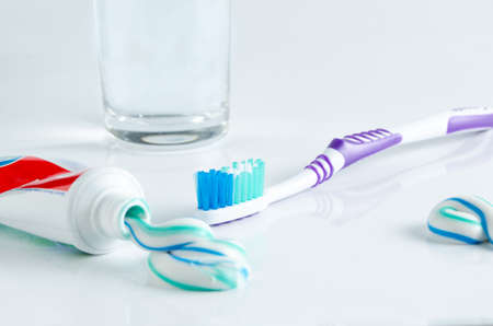 Toothbrush, tube of toothpaste and a glass on a white background