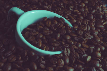 White Cup drowned in roasted coffee beans, toned photoの写真素材