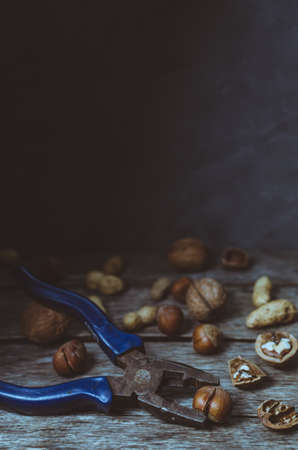 Various nuts, peanuts, hazelnuts and walnuts on old wooden table with tongs, tinted photo