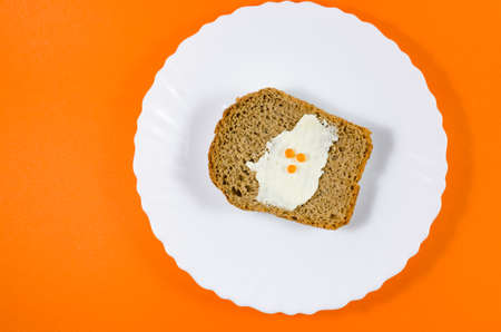 A piece of black rye bread on a white plate, greased with butter and red caviar with orange backgroundの写真素材
