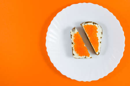 Cut a piece of black rye bread on a white plate, greased with butter and red caviar with orange...