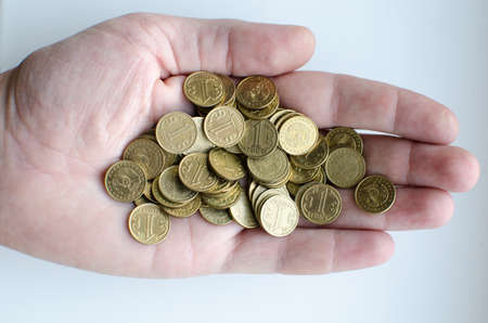 Hand man holding a lot of coins with a nominal value of one tenge on a light background