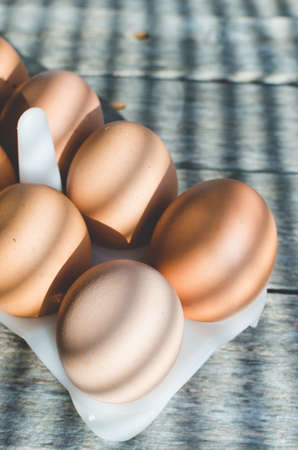 Chicken eggs on a wooden old table in the early sun. The shadows from the blinds fall on the background and eggs.の写真素材