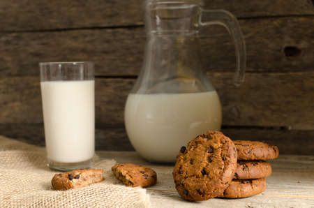 Oatmeal chocolate chip cookies, jug and glass of milk, rustic wooden background. Country dinner.