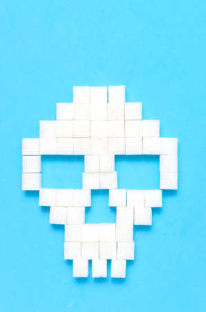 Refined sugar on blue background.Sugar cubes in form of skull.Concept of healthy eating, addiction to candy.Closeup.の写真素材