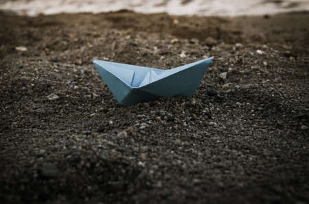 Blue paper boat on the ocean in sand on a cloudy autumn day.の写真素材