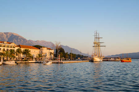 Sailboat with lowered sails is moored in Adriatic port,buildings with tiled roofs and palm trees.の写真素材
