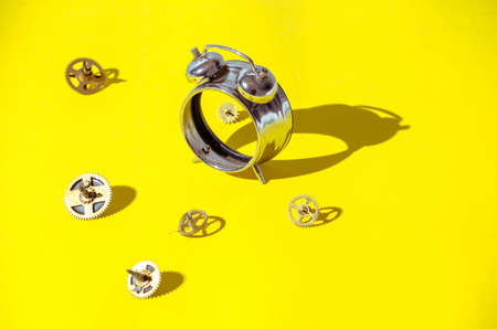 Old alarm clock disassembled into gears on a bright yellow background with hard shadows.View from...
