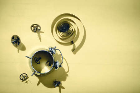Old alarm clock disassembled into gears on a bright yellow background with hard shadows.View from top.の写真素材