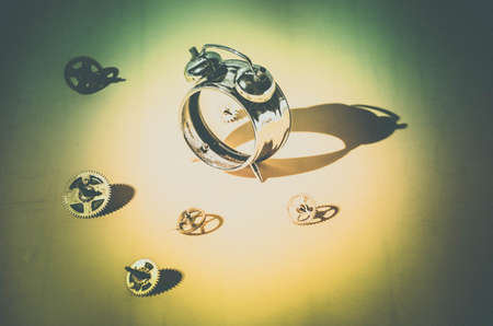 Disassembled alarm clock and scattered gears in bright light with hard shadows.Yellow green background.の写真素材