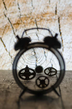 Broken alarm clock with the gears on the background of wood rings. Close up.の写真素材