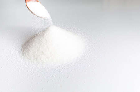 Pile of sugar sand is poured with a wooden spoon on a light background.の写真素材