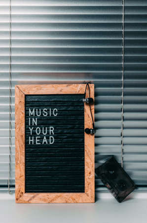 Letter board with the inscription music in your head in white letters on black.Headphones and audio cassette. Background of metal blinds.の写真素材