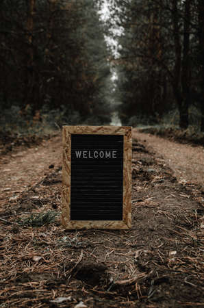 Letter board with white inscription welcome.In forest on the road, travel and tourism.