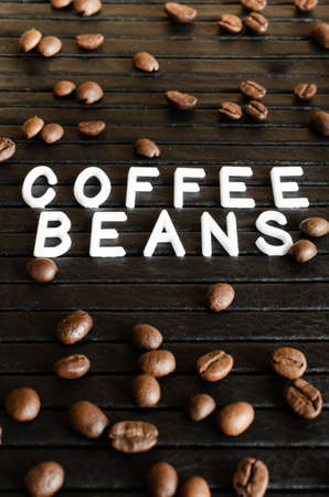 White lettering coffee beans and coffee seeds on black background under tilt.の写真素材