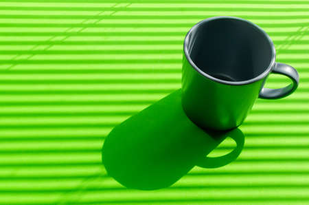 Grey mug on a green background with hard shadows from the rays of the bright sun making its way through the blinds.の写真素材