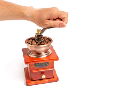 Hand turns the handle of a wooden coffee grinder on a white background.