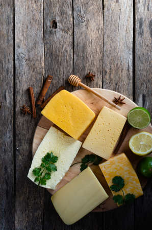 Large variety of cheese with lemon and lime laid on a round cutting Board, also parsley, spices and...