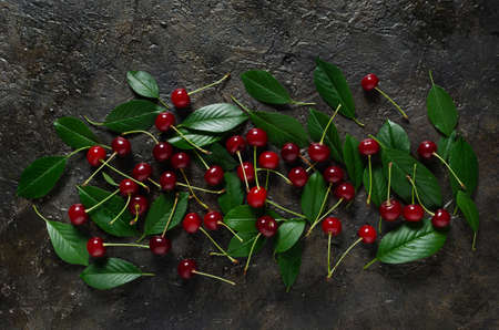 Ripe, bright cherry with green leaves on an old, rustic stone background with a view from the top.
