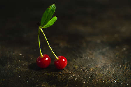 Pair of cherries with green leaves on the old, stone, rustic floor.