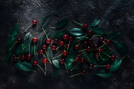 Ripe, bright cherry with green leaves on an old, rustic stone background with a view from the top.