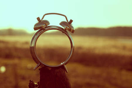 Old alarm clock on the background of the sun, fields and mountains in retro style.の写真素材