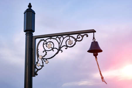 Small bell on a metal openwork pole, against the background of a bright sunset.の写真素材