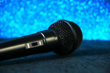 Black microphone fell to the black wooden floor.Against the bright blue bokeh.Musical instrument for singing and karaoke.の写真素材