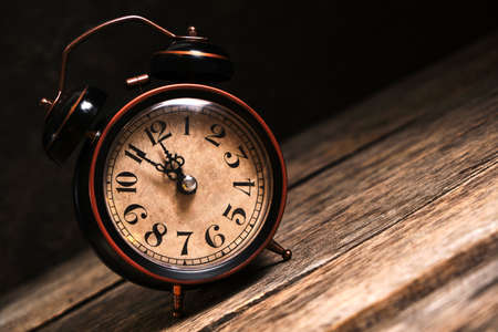 An old, vintage, retro alarm clock on a wooden table rolls off a slanted table.の写真素材