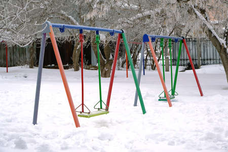 Children Playground with swings, in winter, covered with snowの写真素材