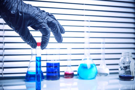 Lab employee in black medical gloves holds a test tube with a blue liquid.