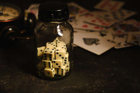 Bottle with dice on table in an underground casino on background of card and an abandoned alarm clockの写真素材