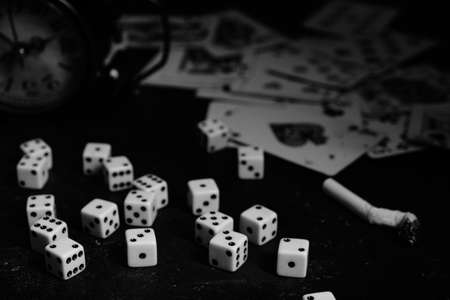 Dice,cigarettes, cards, and an abandoned alarm clock on a table in an underground casino.In black...