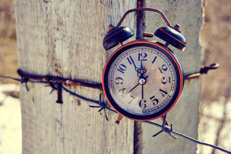 Old retro alarm clock on post tied with barbed wire symbolizes arrival of spring