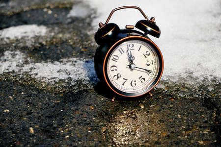 Old retro alarm clock on the melting snow in springの写真素材