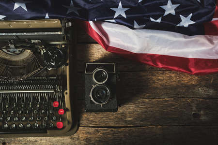 Old retro typewriter, a vintage camera, and the flag of the United States of America on a wooden tableの写真素材