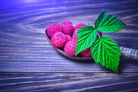 Raspberry berry in a wooden spoon and a green raspberry leaf on a dark backgroundの写真素材
